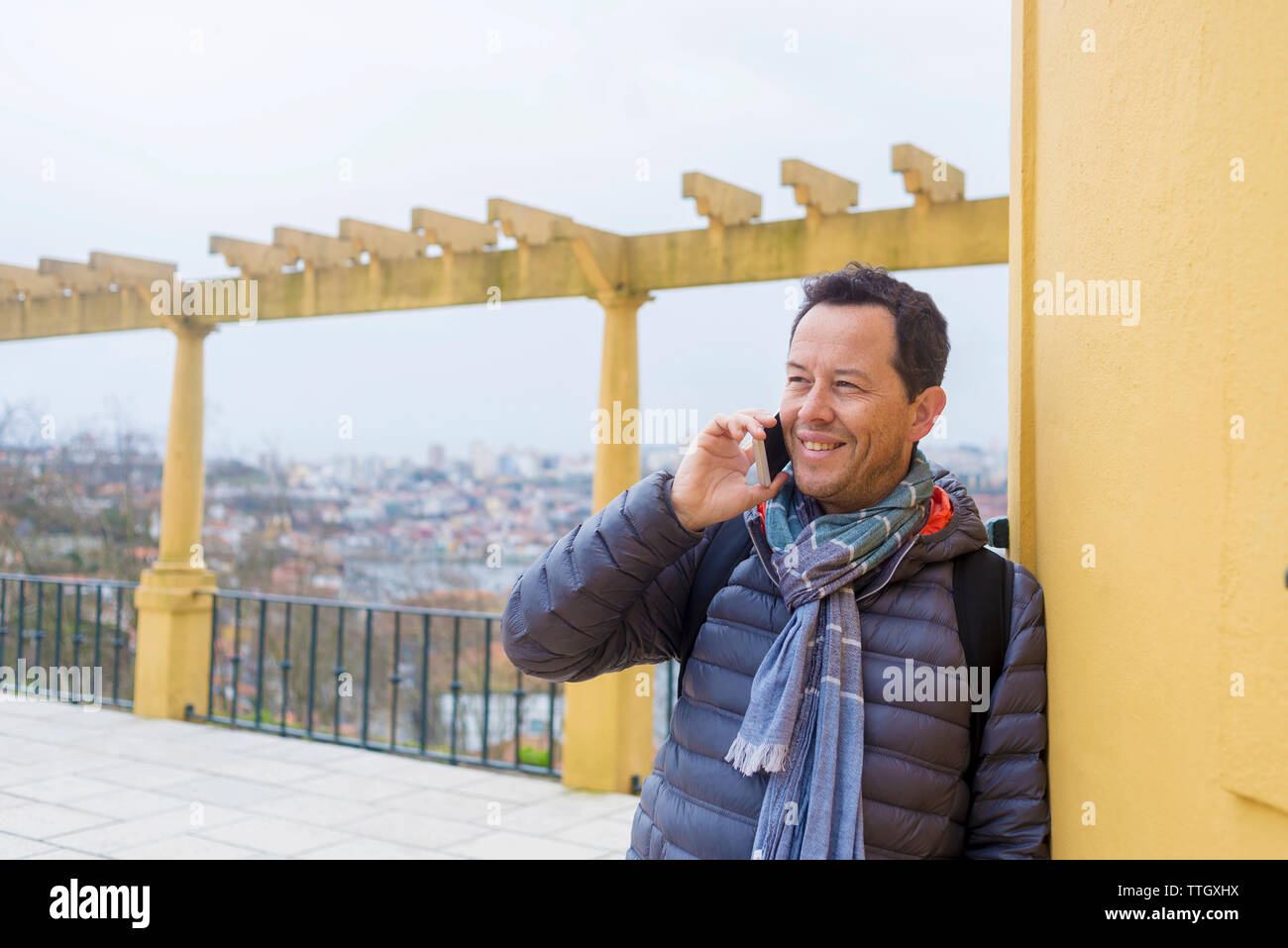 Sorridente turista indossando un abbigliamento caldo rispondendo alle smart phone mentre guarda lontano in città Foto Stock