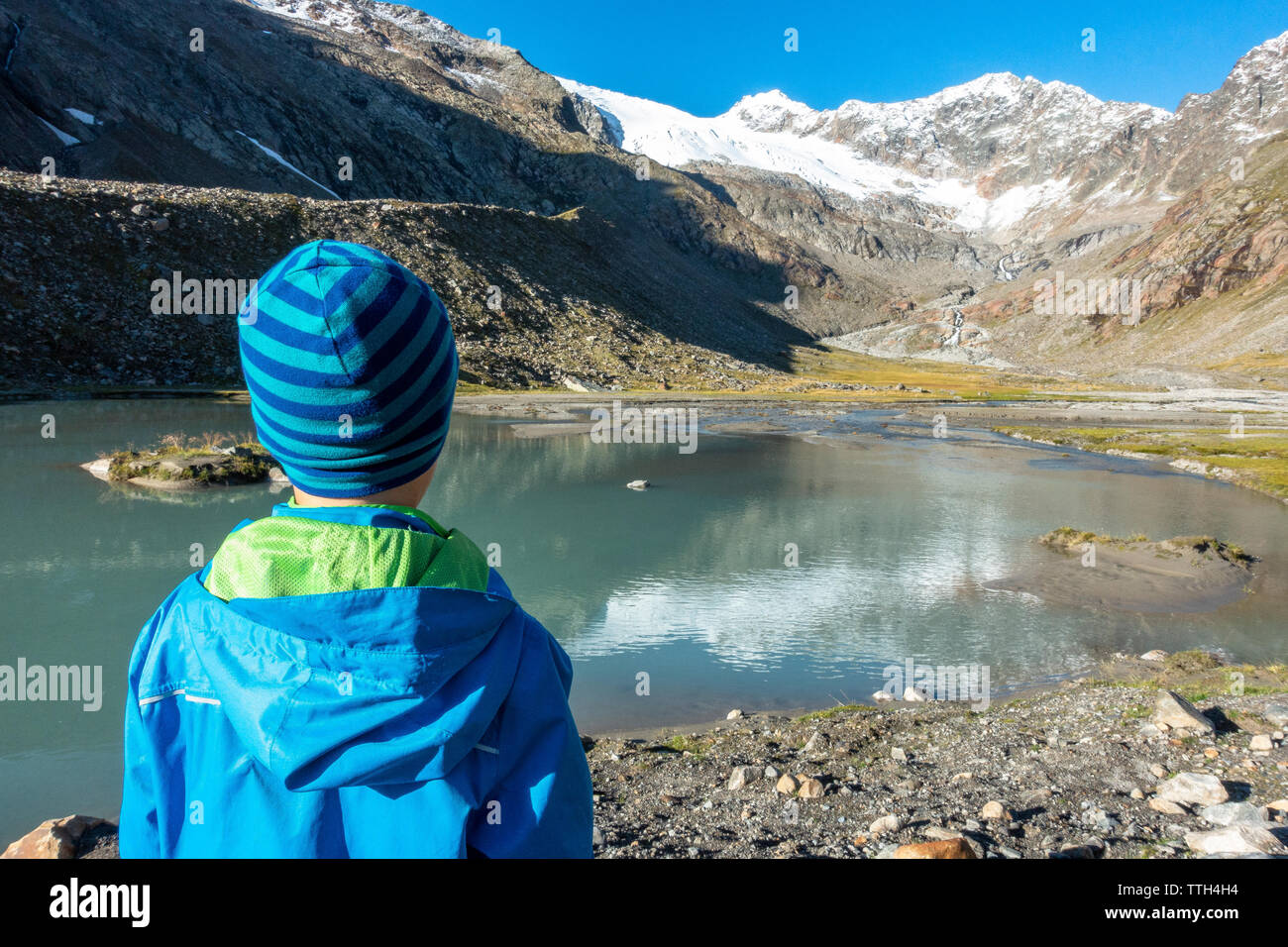 Giovane ragazzo in piedi di fronte ad un lago di montagna e godendo della vista Foto Stock