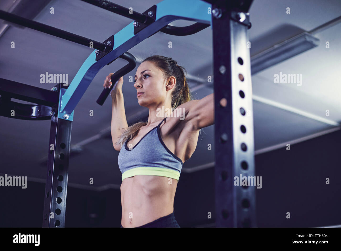 Profilo anteriore della giovane donna facendo chin ups al centro fitness Foto Stock