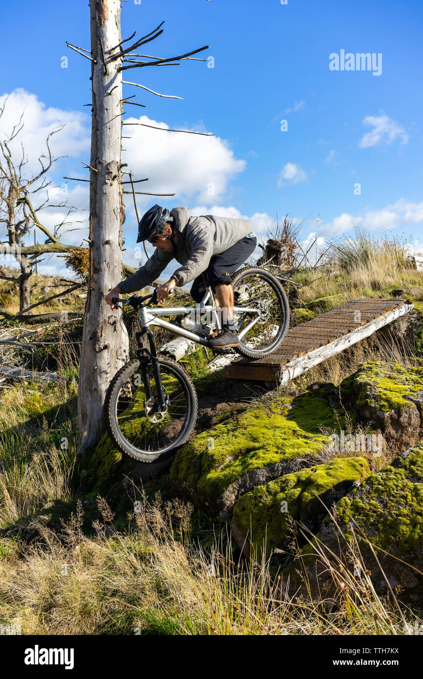 Mountain Biker rolling off bridge in moss rocce coperte Foto Stock