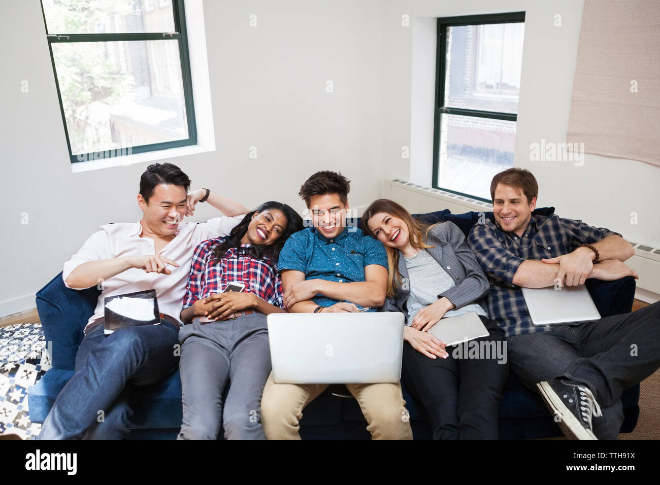 Allegro la gente di affari con computer portatile mentre vi rilassate sul divano in office Foto Stock
