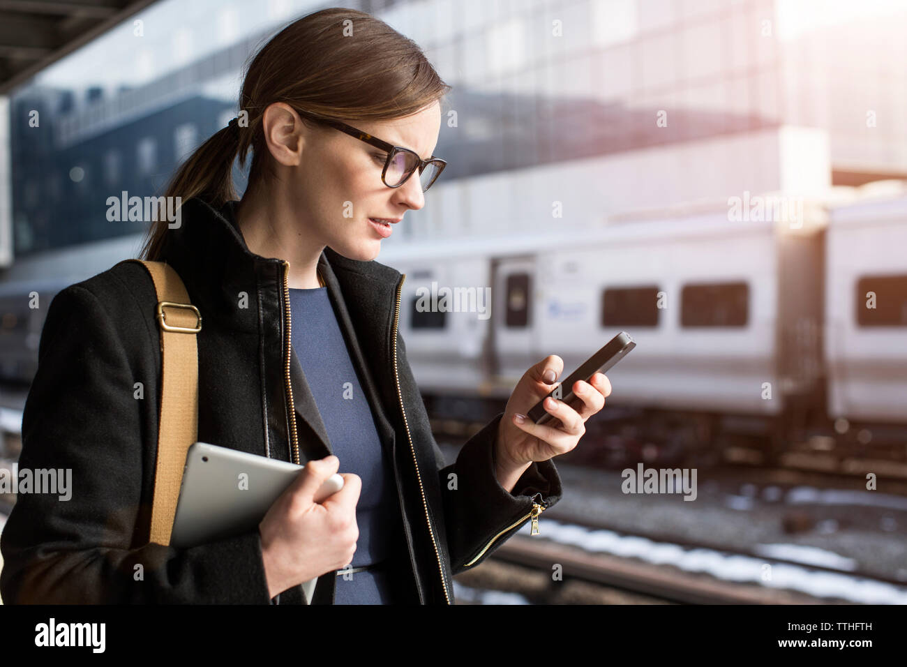 Giovane imprenditrice della messaggistica di testo mentre in piedi alla stazione ferroviaria Foto Stock