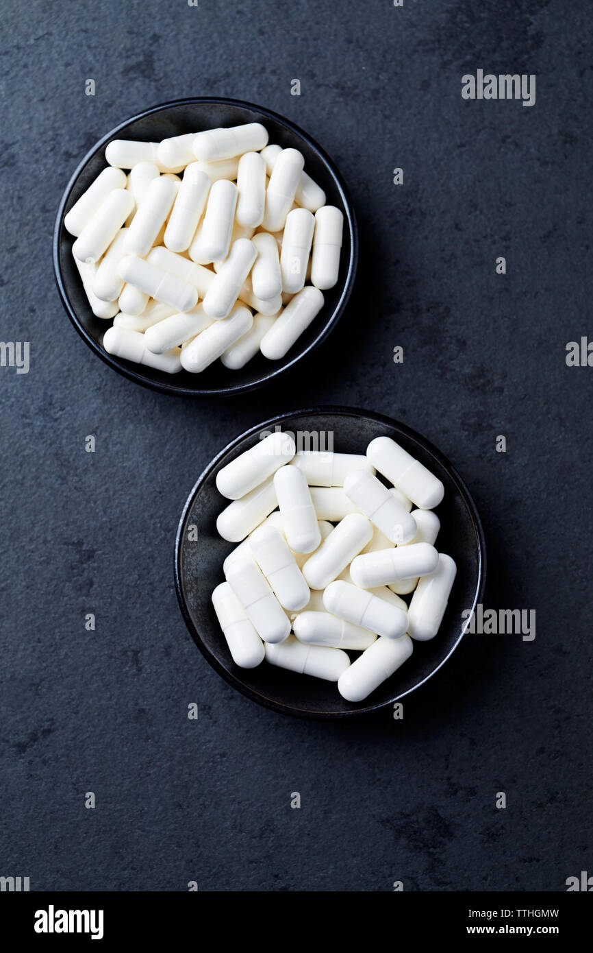 Arginina alfa-chetoglutarato (AAKG) e creatina capsule. Bodybuilding integratori alimentari in pietra scura sullo sfondo. Vista dall'alto. Copia dello spazio. Foto Stock