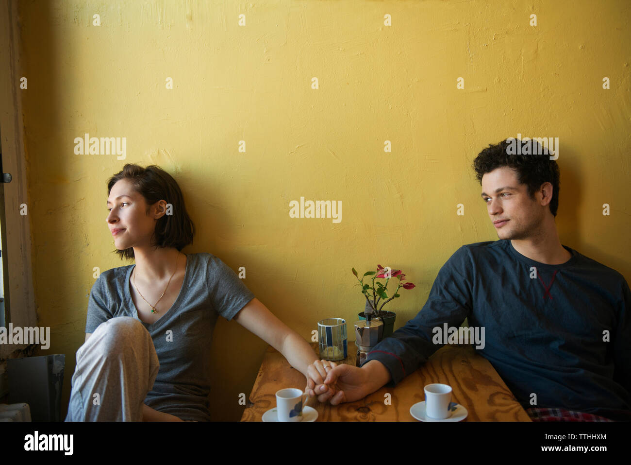 Coppia sorridente tenendo le mani sul tavolo contro la parete Foto Stock Coppia sorridente tenendo le mani sul tavolo contro la parete Foto Stock