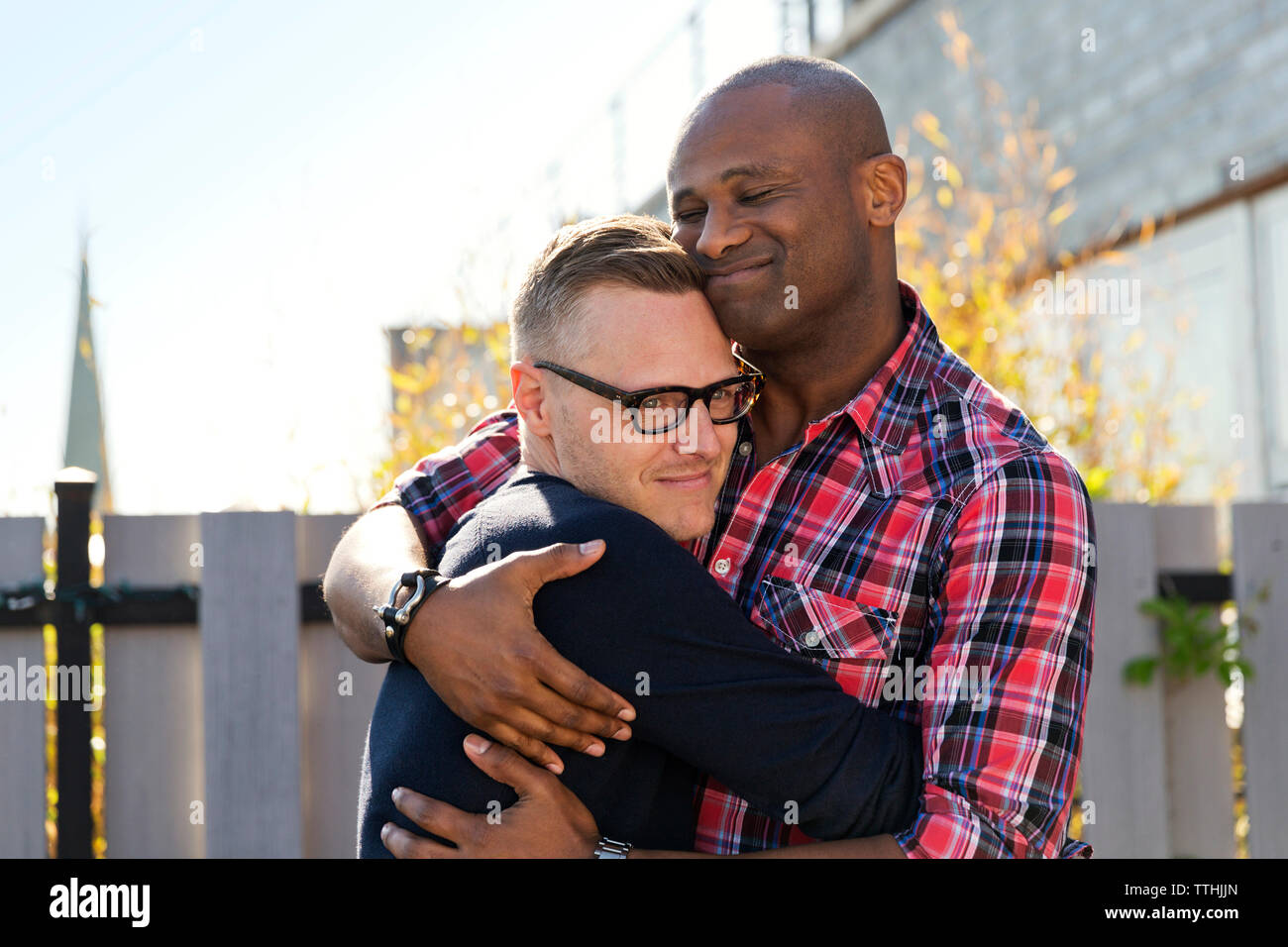 Sorridente uomini gay abbracciando contro la recinzione Foto Stock