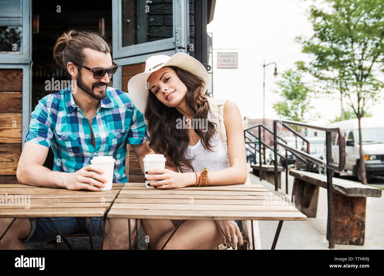 Coppia felice azienda tazze monouso e seduta al tavolo al cafè sul marciapiede Foto Stock