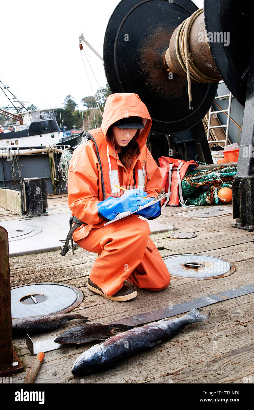 Donna pesci di controllo e scrittura su appunti in barca da pesca Foto Stock