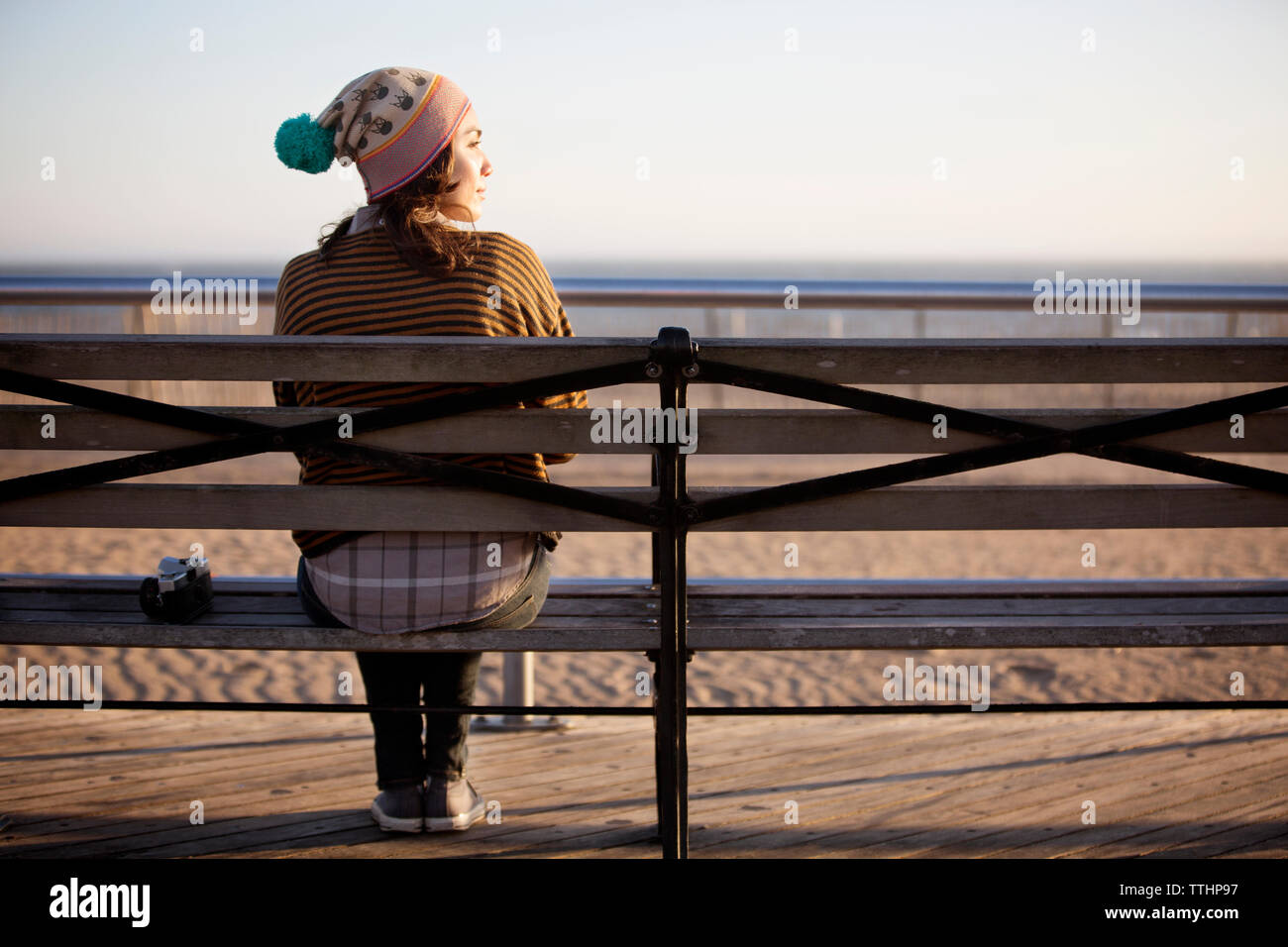 Vista posteriore della donna seduta su un banco di lavoro contro la spiaggia Foto Stock