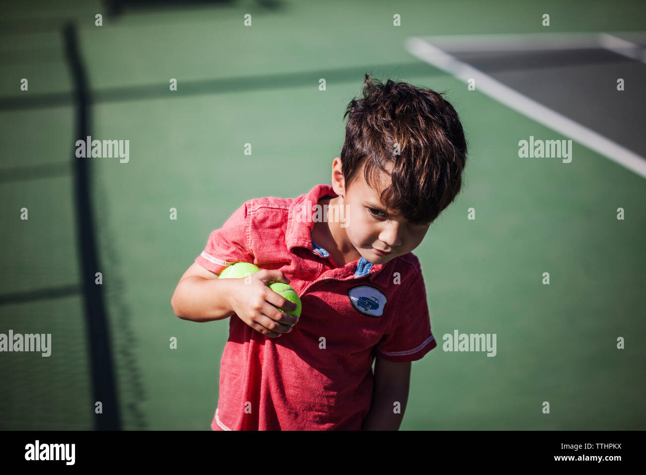 Curioso Ragazzo che guarda lontano tenendo le palline da tennis su corte Foto Stock