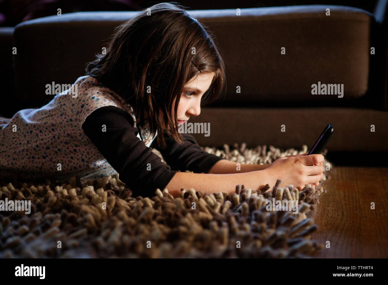 Ragazza utilizzando il telefono cellulare mentre giaceva sul tappeto a casa Foto Stock