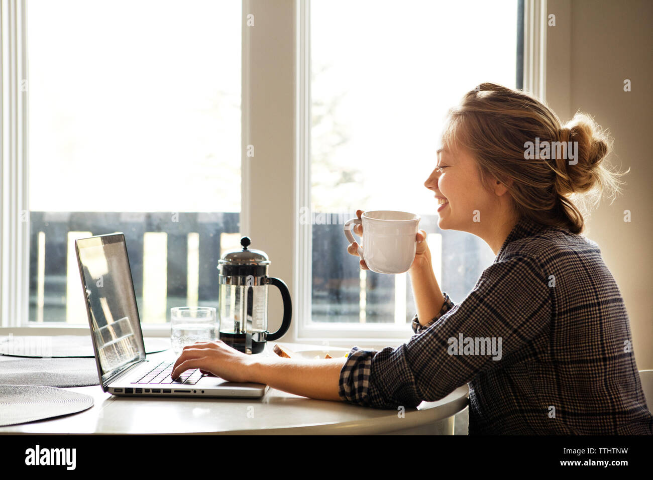 Donna felice utilizzando computer portatile mentre si gusta un caffè a tabella Foto Stock
