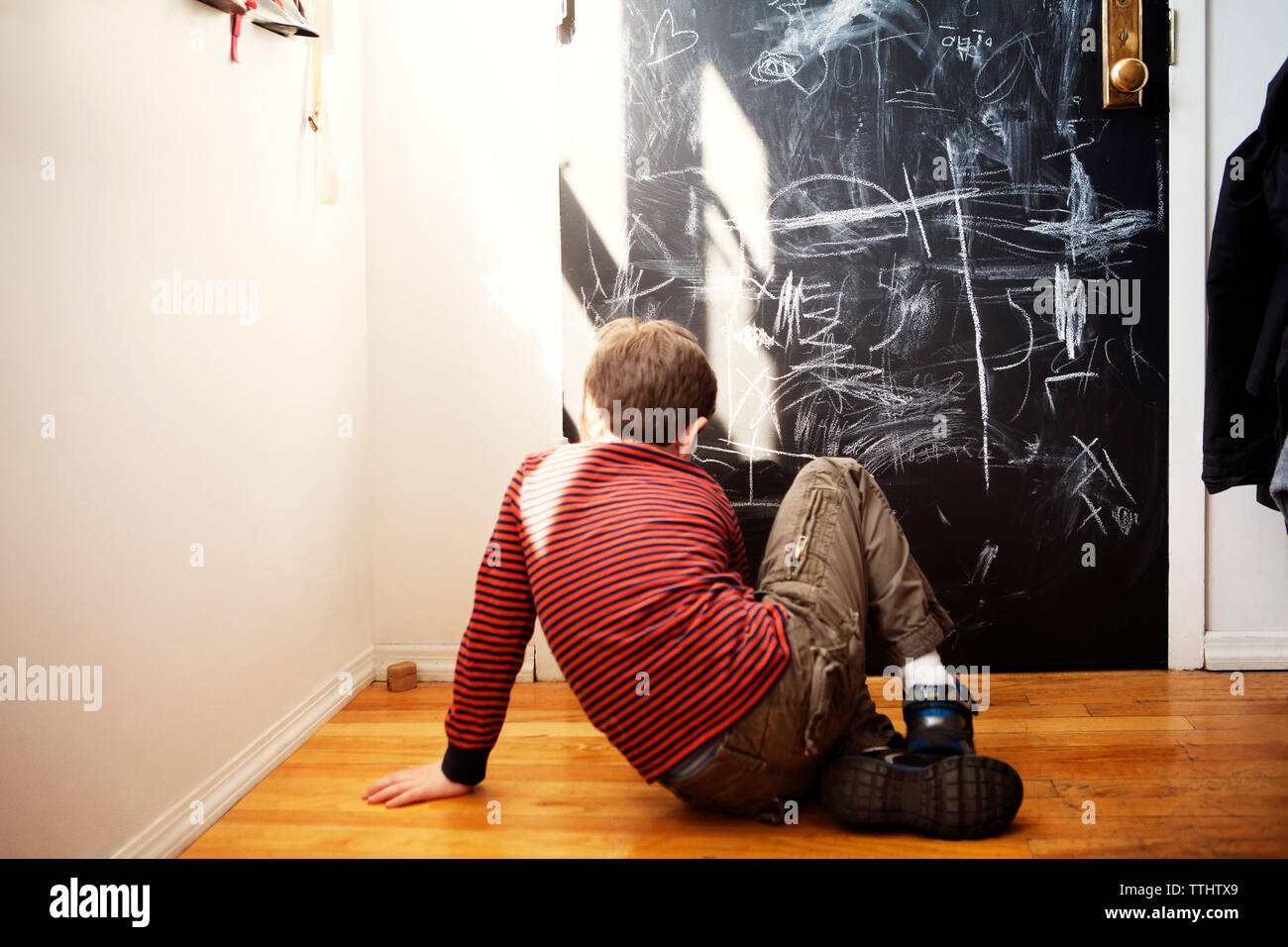 Vista posteriore del ragazzo seduto sul pavimento Harwood a casa Foto Stock