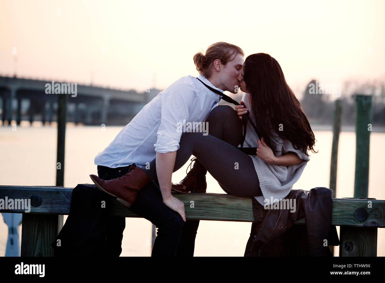 Coppia romantica baciare mentre è seduto sulla ringhiera contro sky Foto Stock