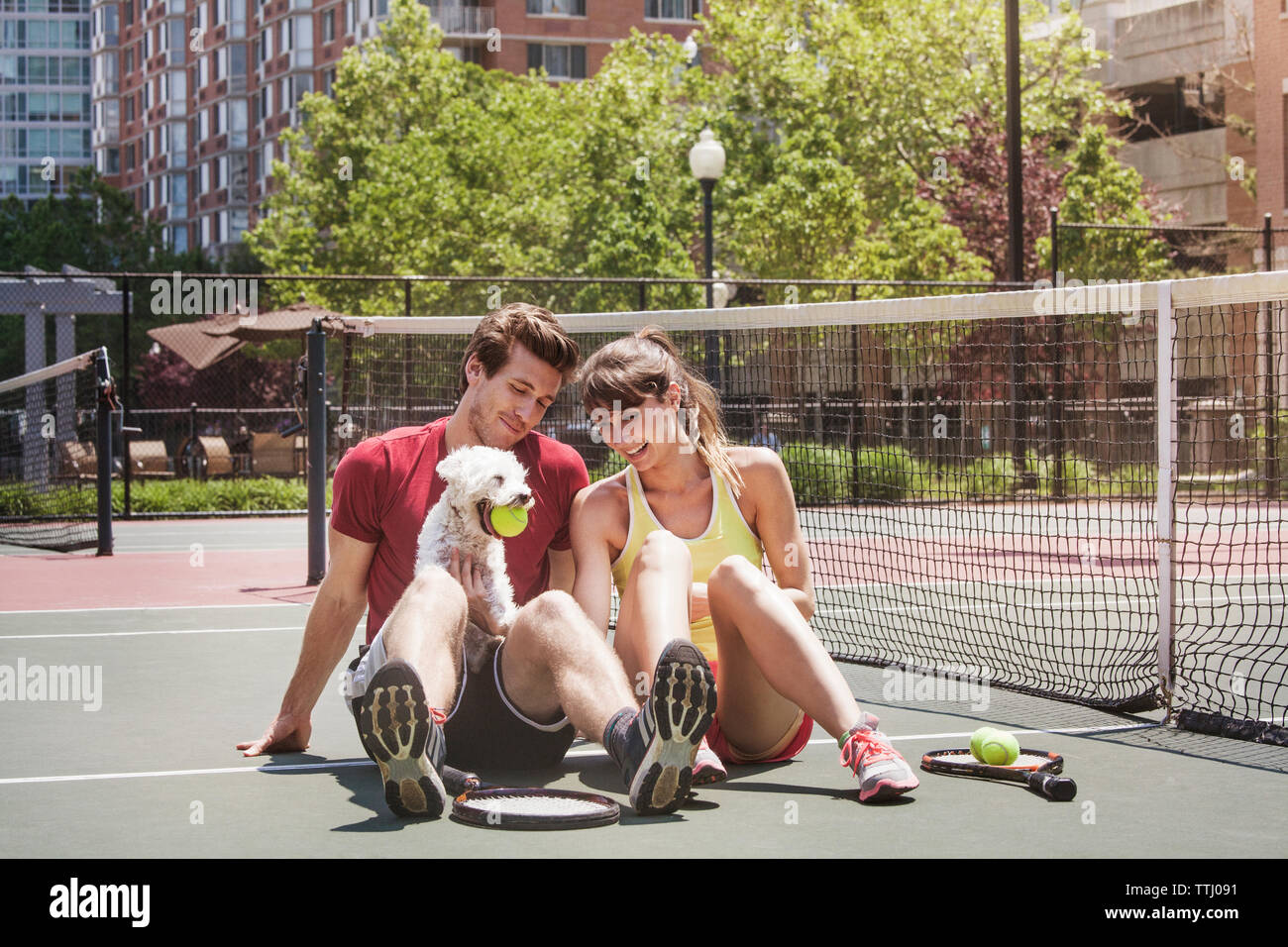 Felice coppia seduta con il cane nel campo da tennis Foto Stock