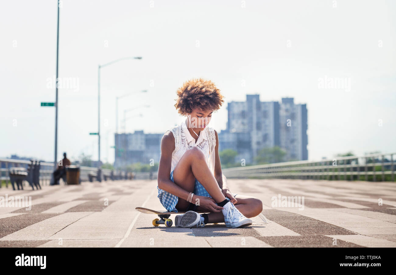 Adolescente ascoltare musica mentre seduto su skateboard Foto Stock