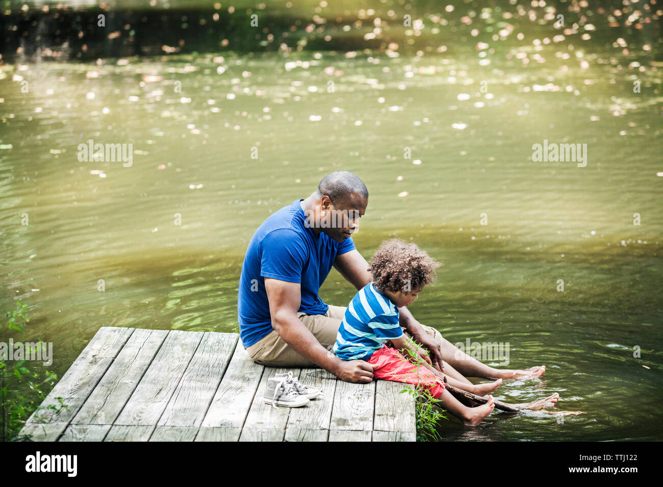 Padre e figlio seduti sul molo con i piedi nel lago Foto Stock