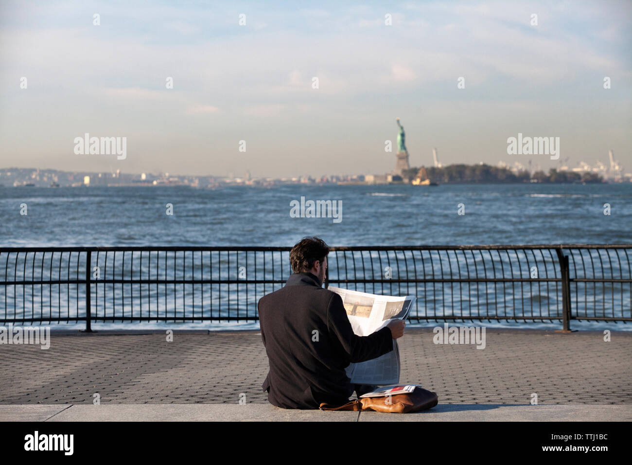 Uomo di lettura carta notizie mentre è seduto sulla promenade contro il fiume Hudson Foto Stock