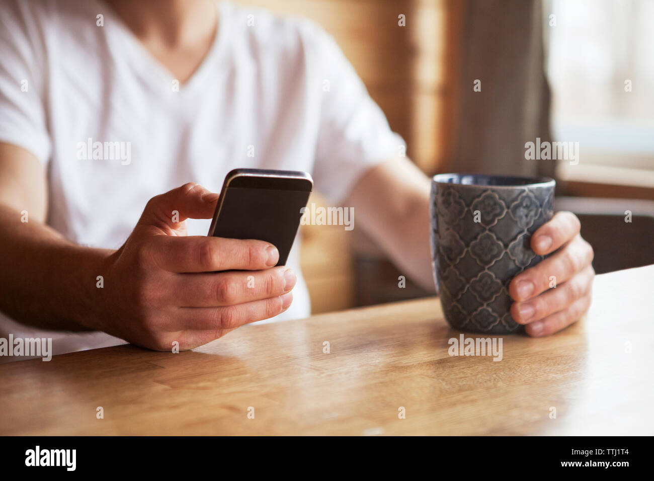Sezione mediana dell'uomo utilizzando il telefono cellulare mentre si tiene tazza di caffè presso il cafe Foto Stock