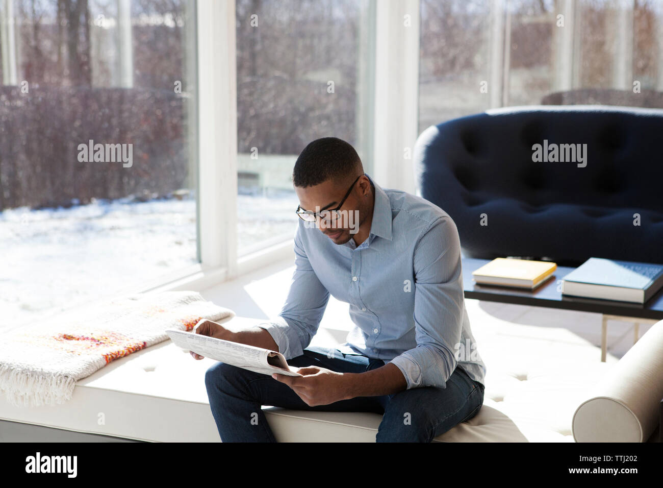 Uomo che legge il giornale mentre è seduto sul divano nel soggiorno Foto Stock