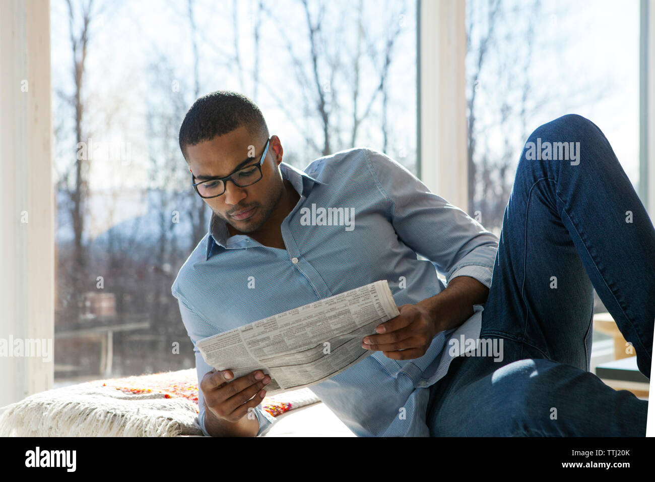 Uomo che legge il giornale comodamente seduti sul divano di casa Foto Stock