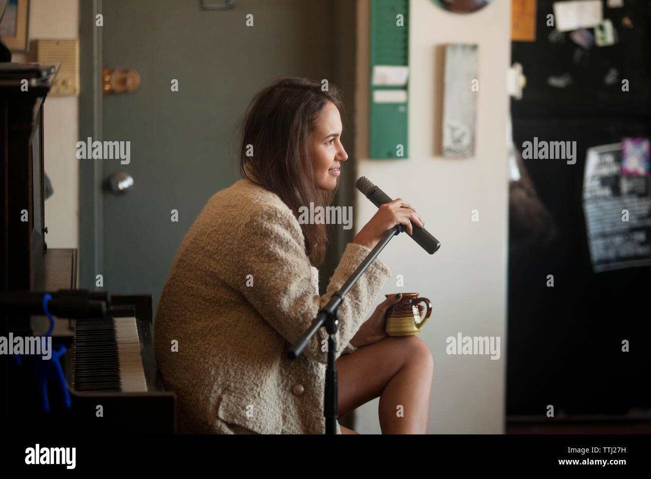Vista laterale della donna tenendo il microfono mentre è seduto a casa Foto Stock