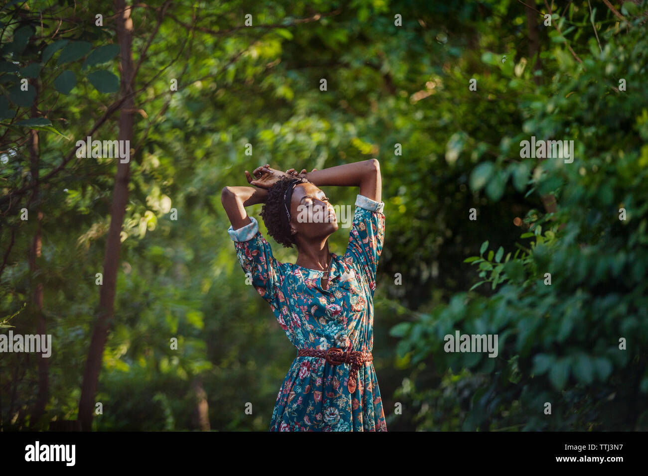 Donna con gli occhi chiusi e braccia alzate in piedi in mezzo di alberi in posizione di parcheggio Foto Stock