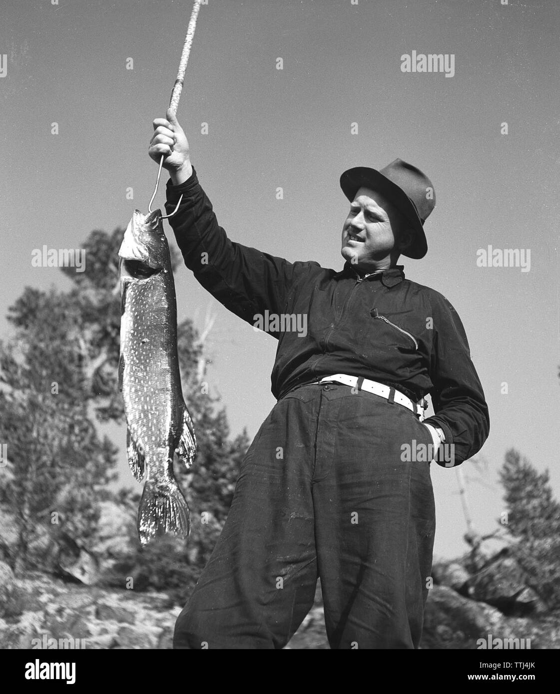 La pesca nel 1940s. Un uomo ha catturato un pesce e lo mostra in alto per il fotografo. La Svezia 1943 Kristoffersson ref F102-1 Foto Stock