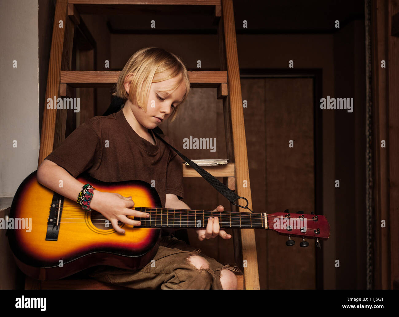 Ragazzo la pratica di chitarra mentre è seduto sulla scaletta a casa Foto Stock