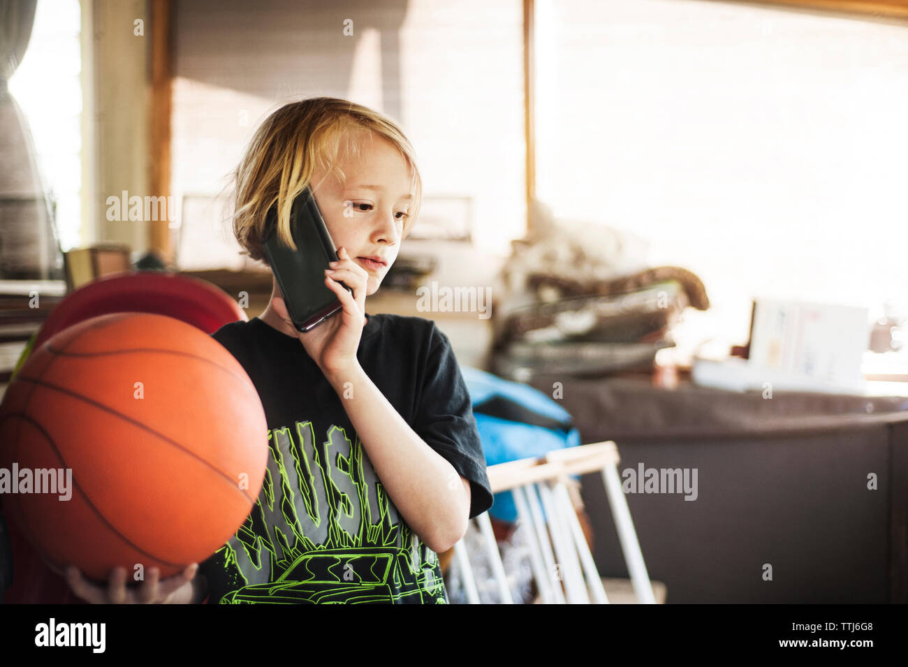 Ragazzo tenendo la pallacanestro mentre parlano al telefono mobile a casa Foto Stock