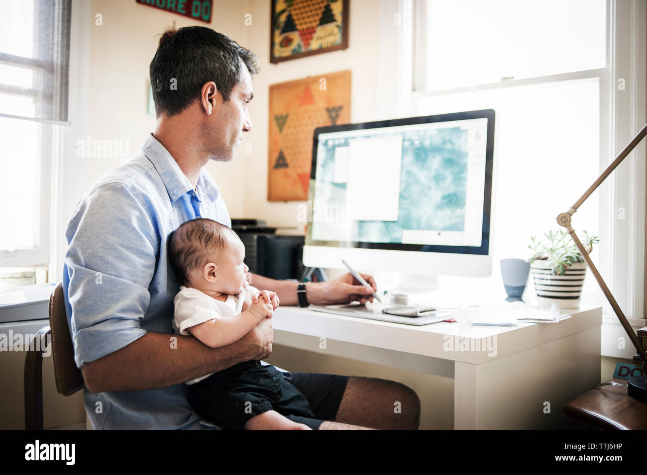 Uomo che porta bambino mentre si lavora su un computer desktop a casa Foto Stock