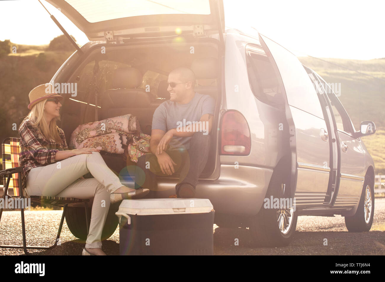 Uomo seduto nel baule auto parlando di donna sulla giornata di sole Foto Stock