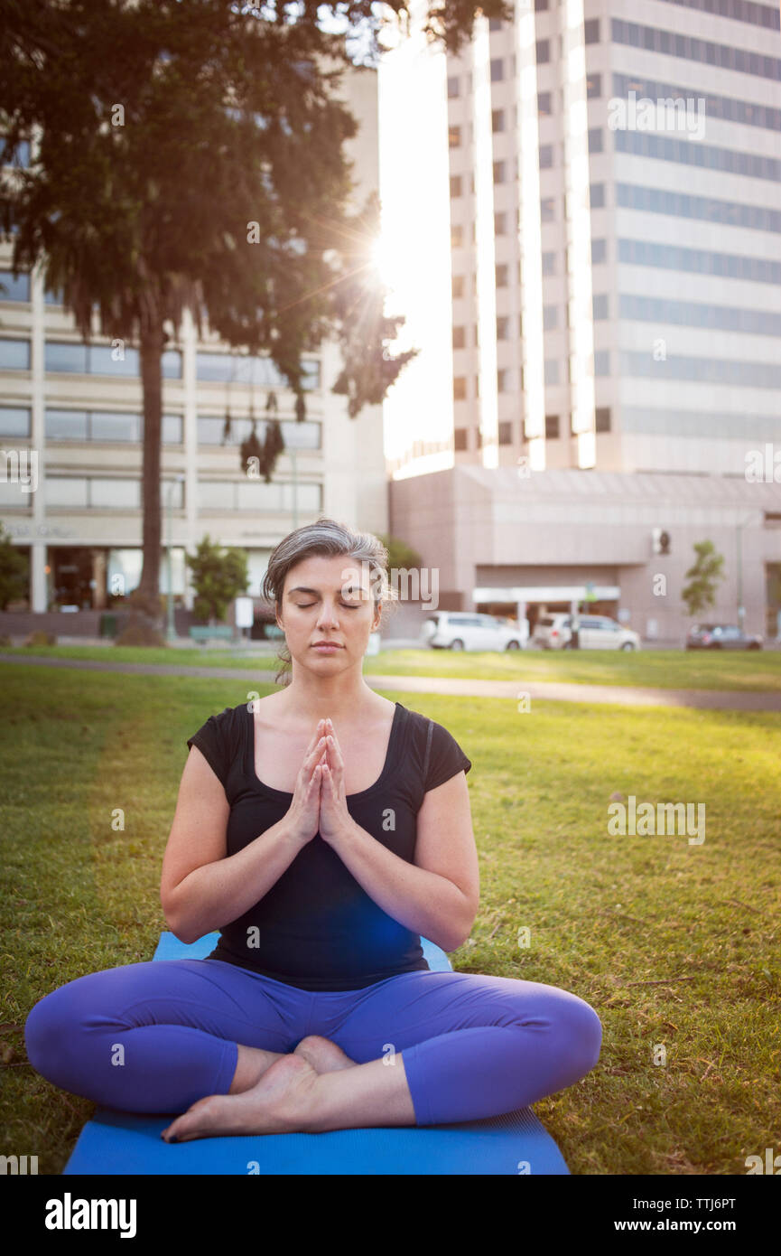 Donna meditando mentre è seduto sul tappeto di esercizio in posizione di parcheggio Foto Stock