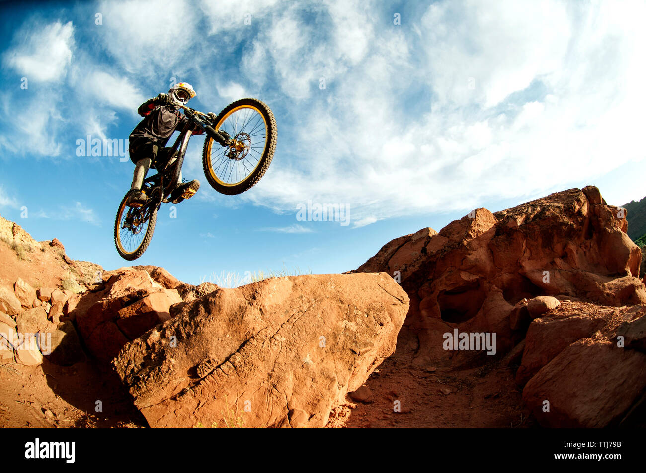 Ciclista jumping dalle rocce contro il cielo nuvoloso Foto Stock