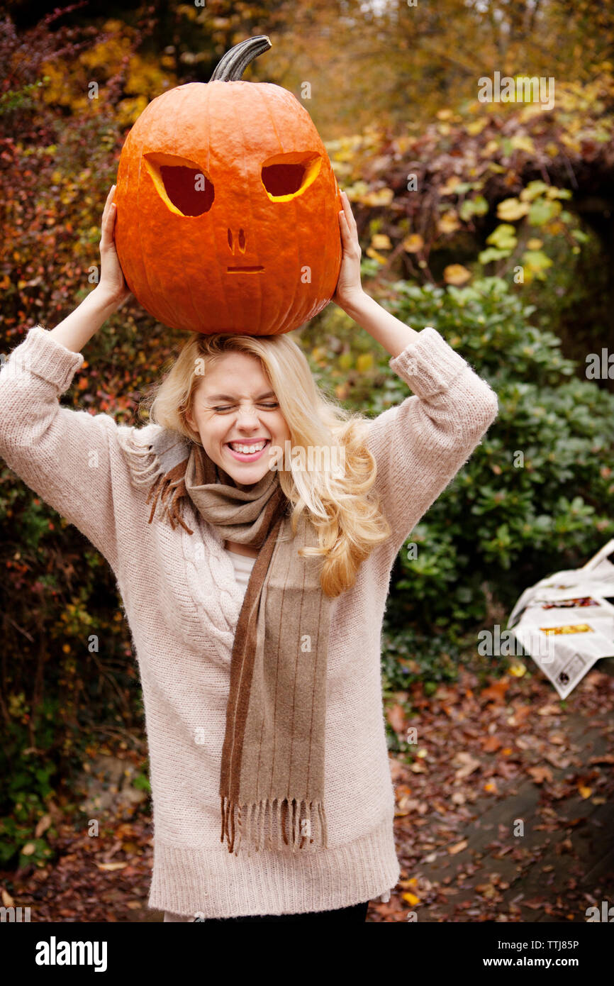 La donna che porta la zucca di Halloween sulla testa mentre si sta in piedi in cortile Foto Stock