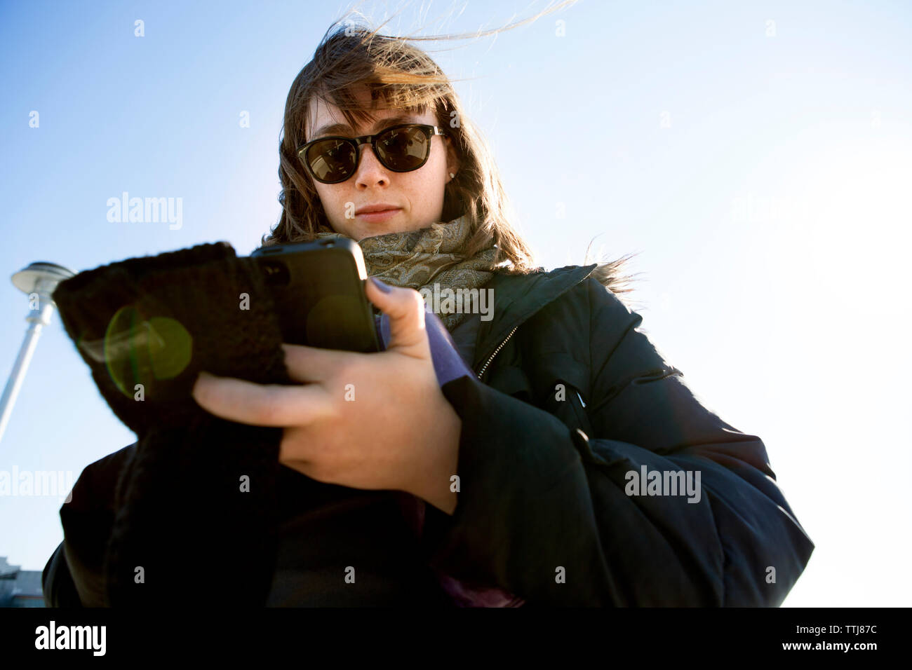 Basso angolo di visione della donna utilizzando smart phone mentre in piedi contro il cielo chiaro Foto Stock