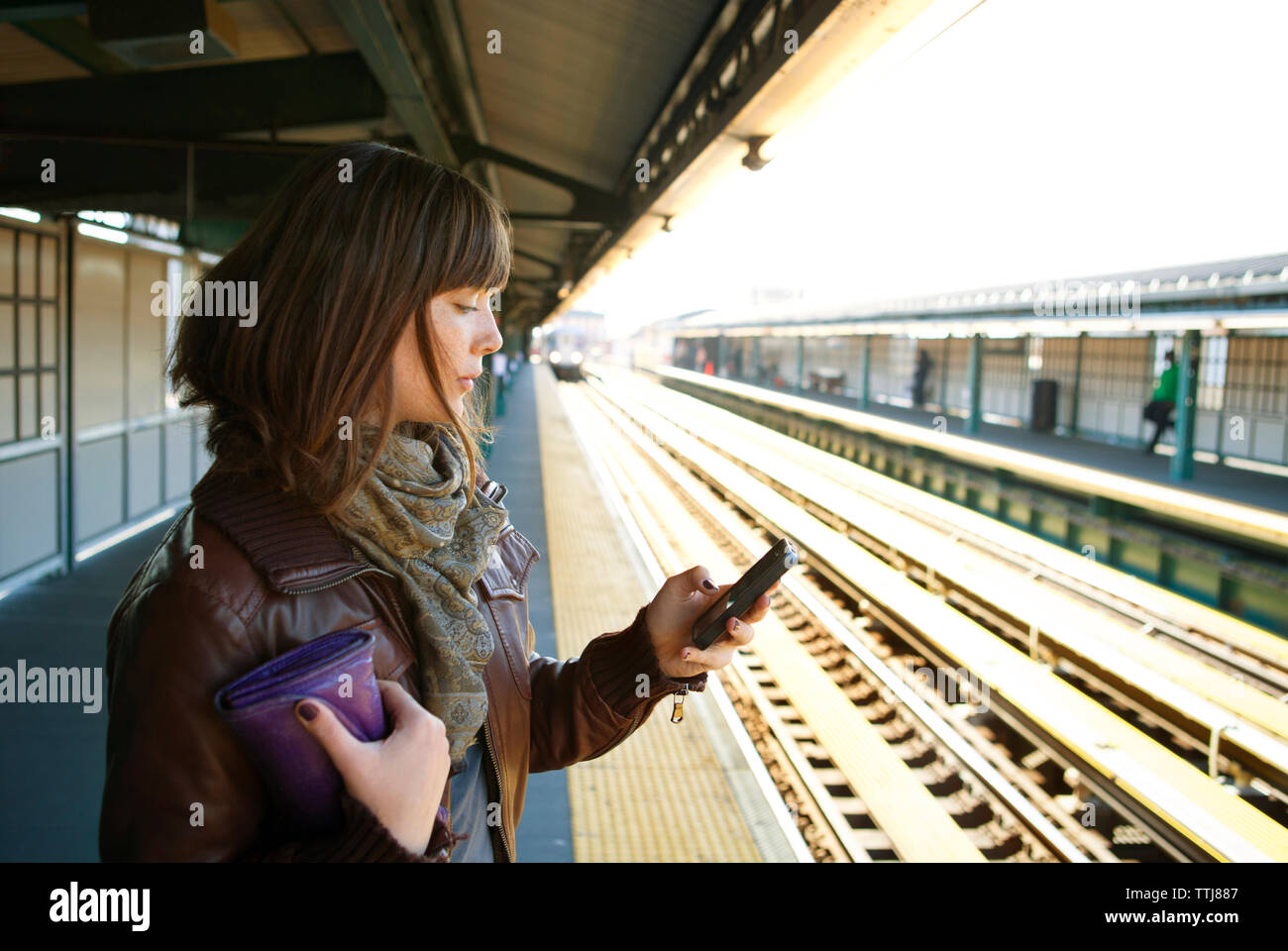 Donna che utilizza smart phone mentre in piedi sulla piattaforma della ferrovia Foto Stock