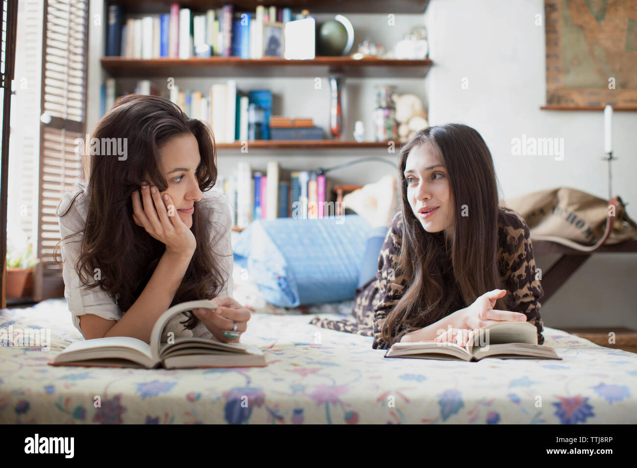 Sorelle di parlare durante la lettura di un libro sul letto Foto Stock
