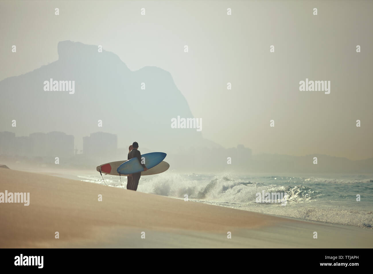 Giovane che trasportano le tavole da surf mentre si sta in piedi in spiaggia Foto Stock
