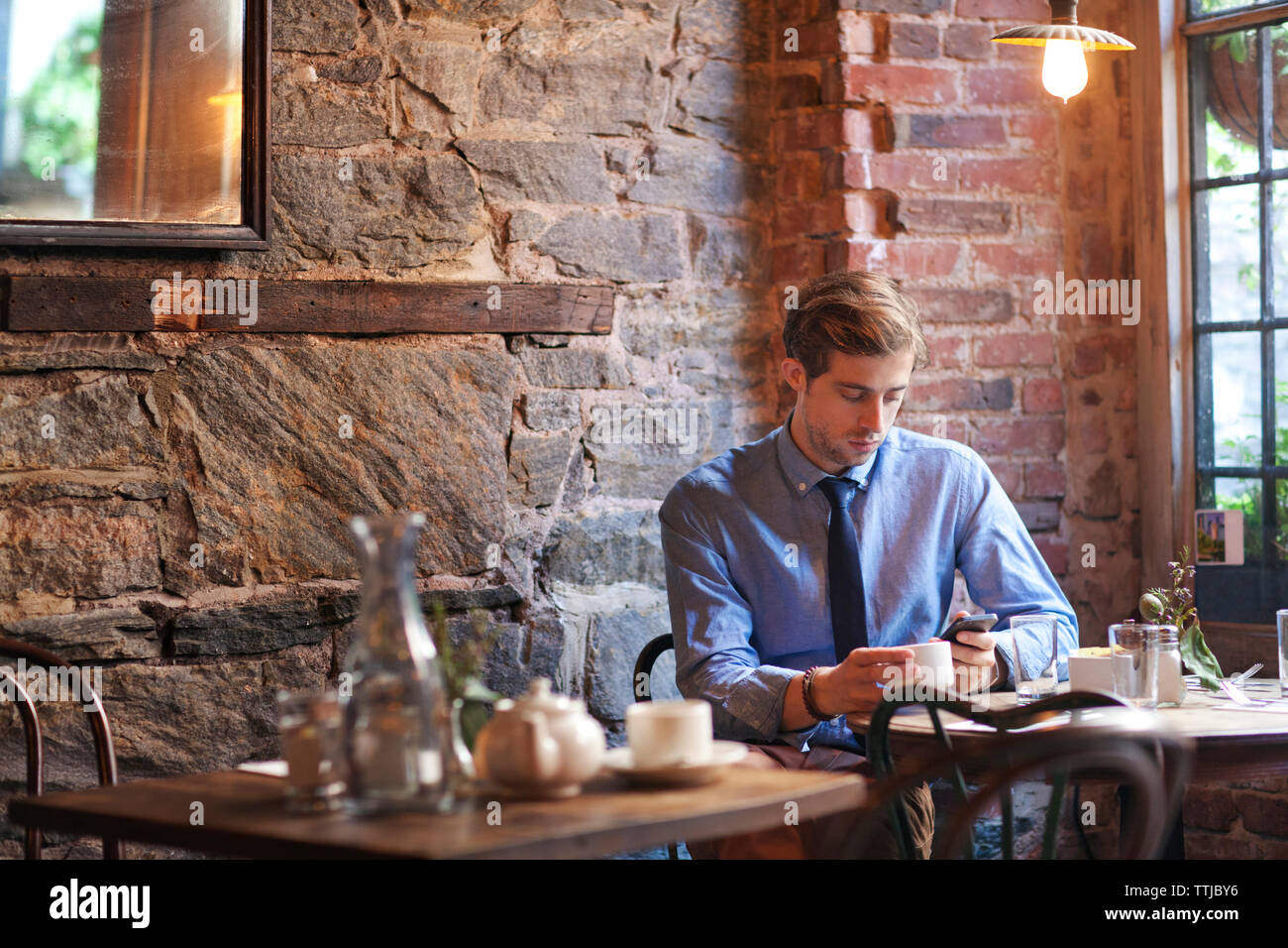 Uomo che utilizza il telefono cellulare mentre è seduto presso il cafe Foto Stock