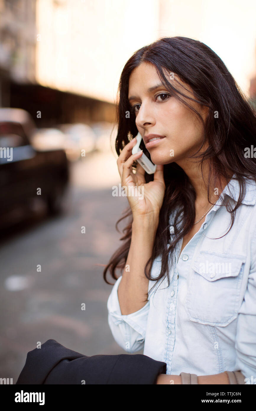 Donna che guarda lontano mentre parlano al telefono intelligente a street Foto Stock
