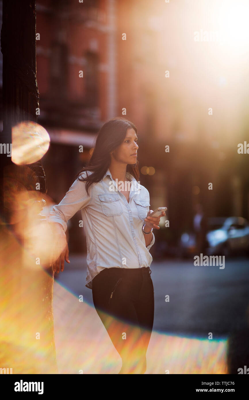 Donna che guarda lontano tenendo premuto smart phone a street Foto Stock