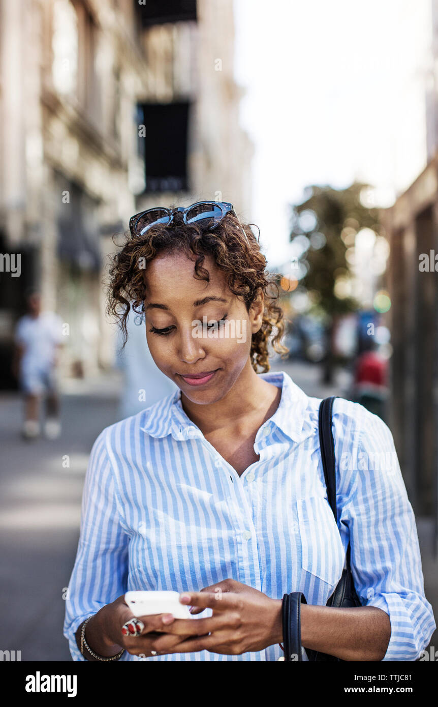 Donna che utilizza il telefono cellulare mentre si sta in piedi in una strada di città Foto Stock