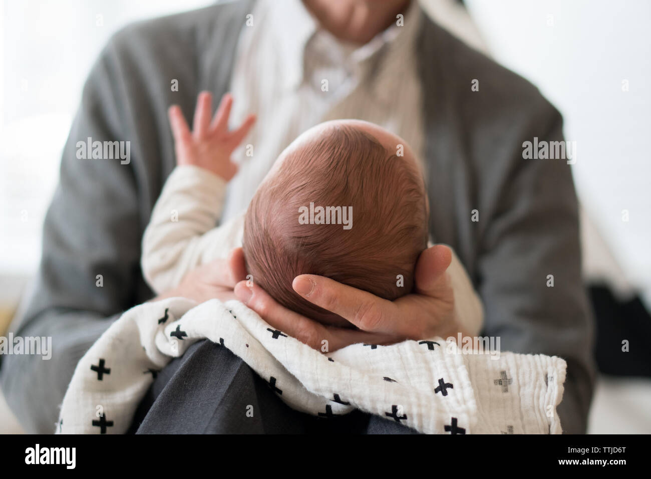 Una prospettiva collo giù di un adulto in una camicia con colletto che culla la testa di un neonato in mano con la mano del bambino sollevata. Foto Stock