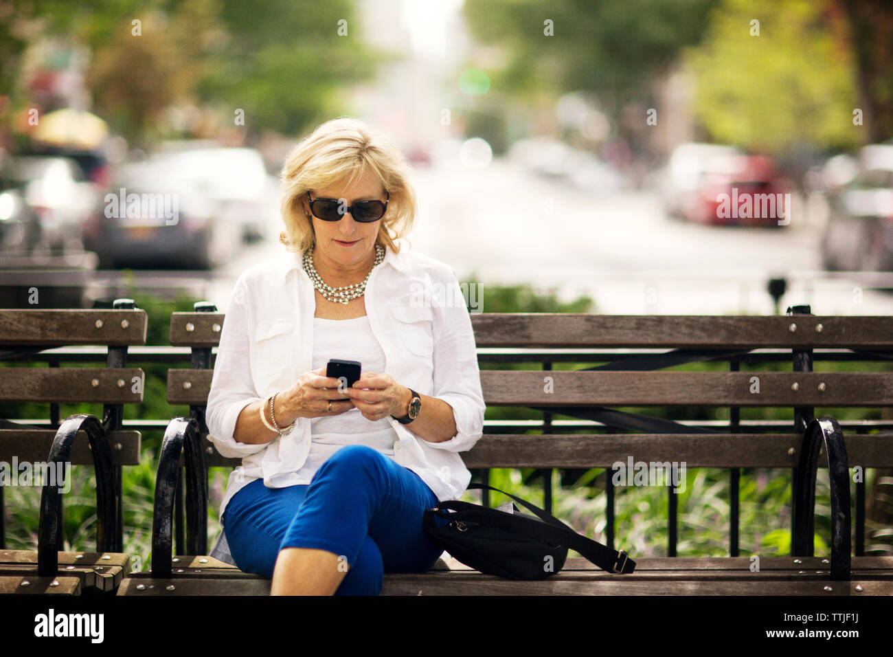 Donna che utilizza il telefono cellulare mentre è seduto sul banco di lavoro Foto Stock
