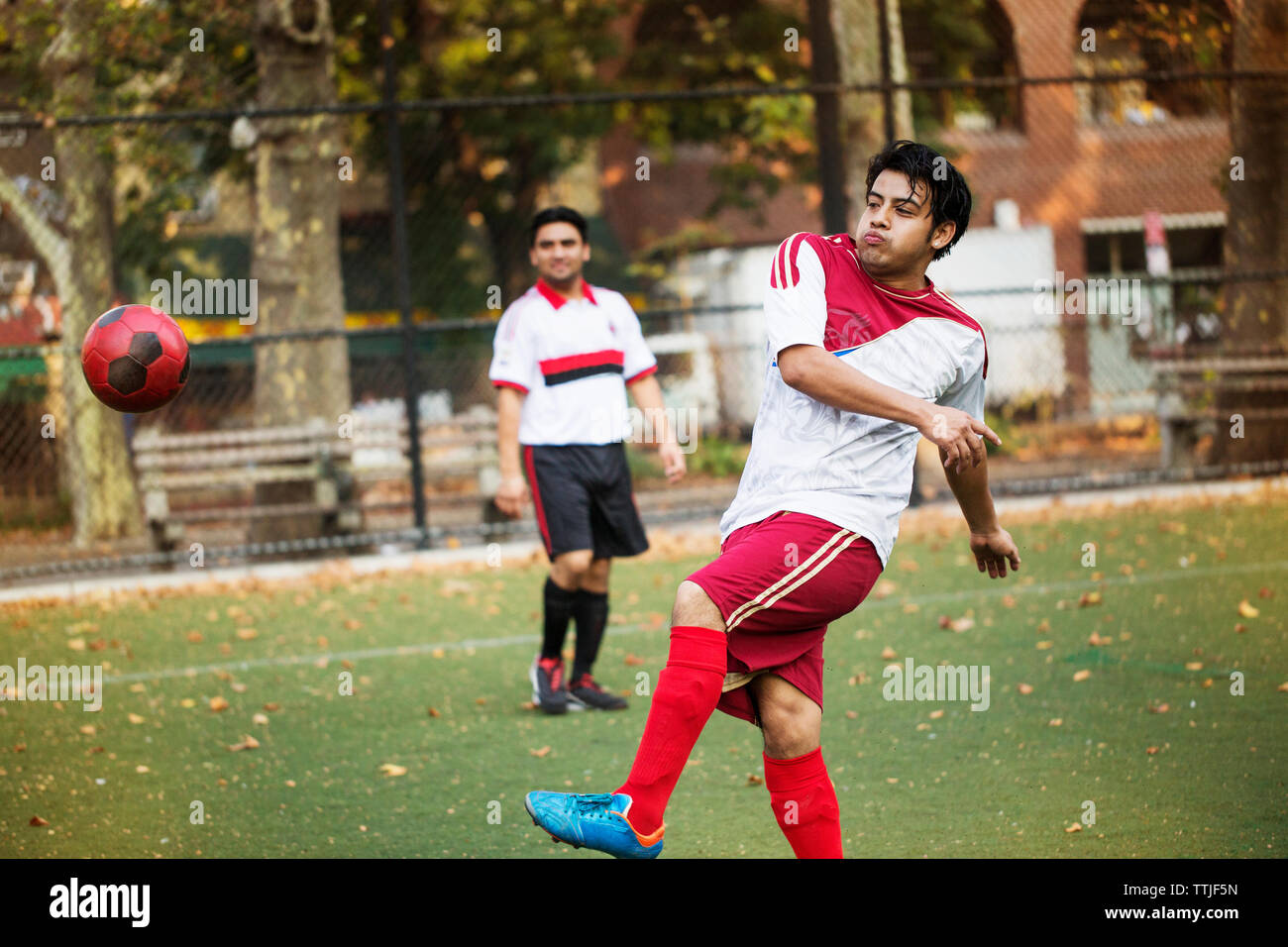 Giocatore di calcio calci palla mentre amico cercando nel campo Foto Stock