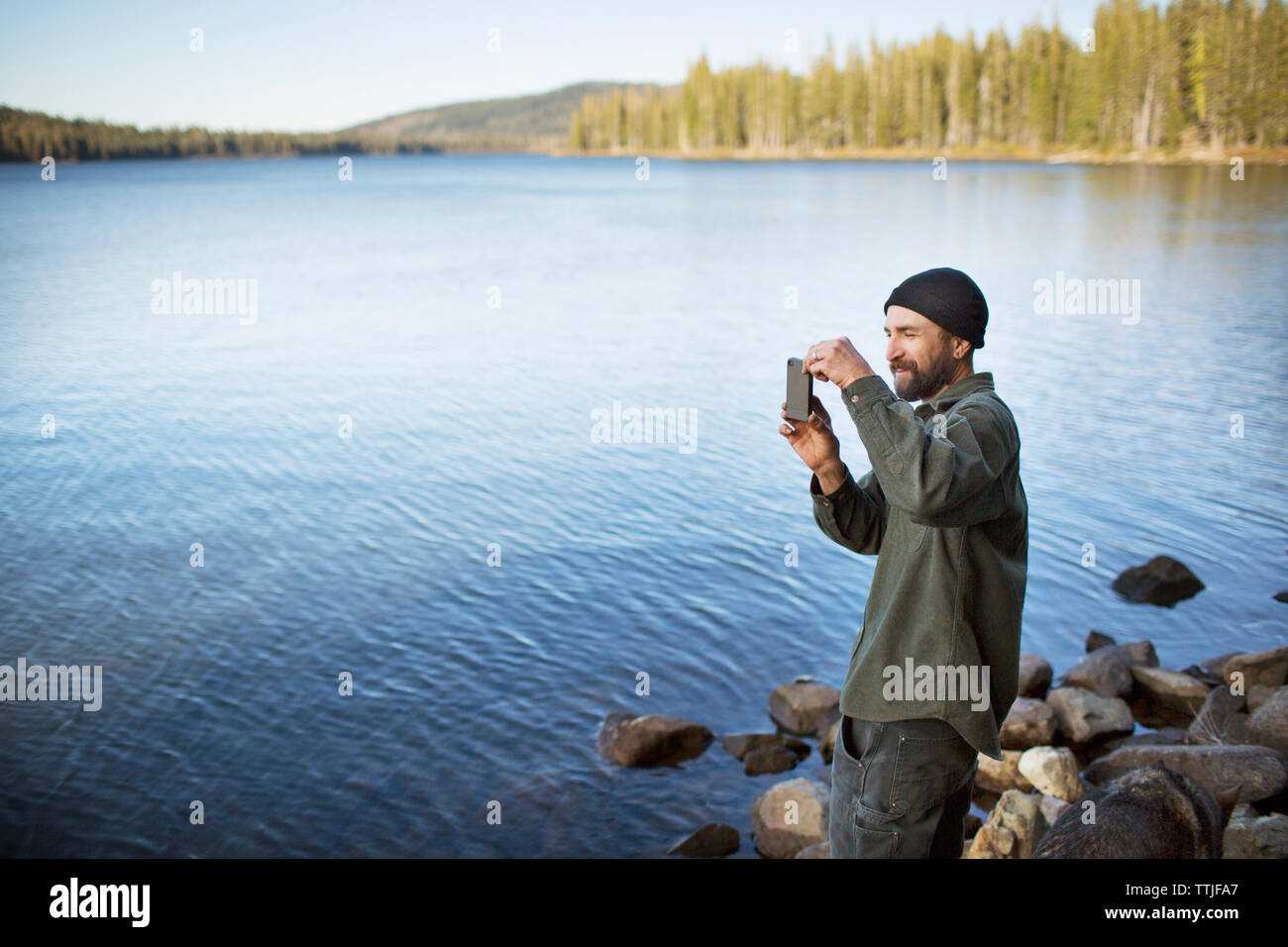 Uomo di fotografare con il cellulare mentre in piedi sul lungolago Foto Stock