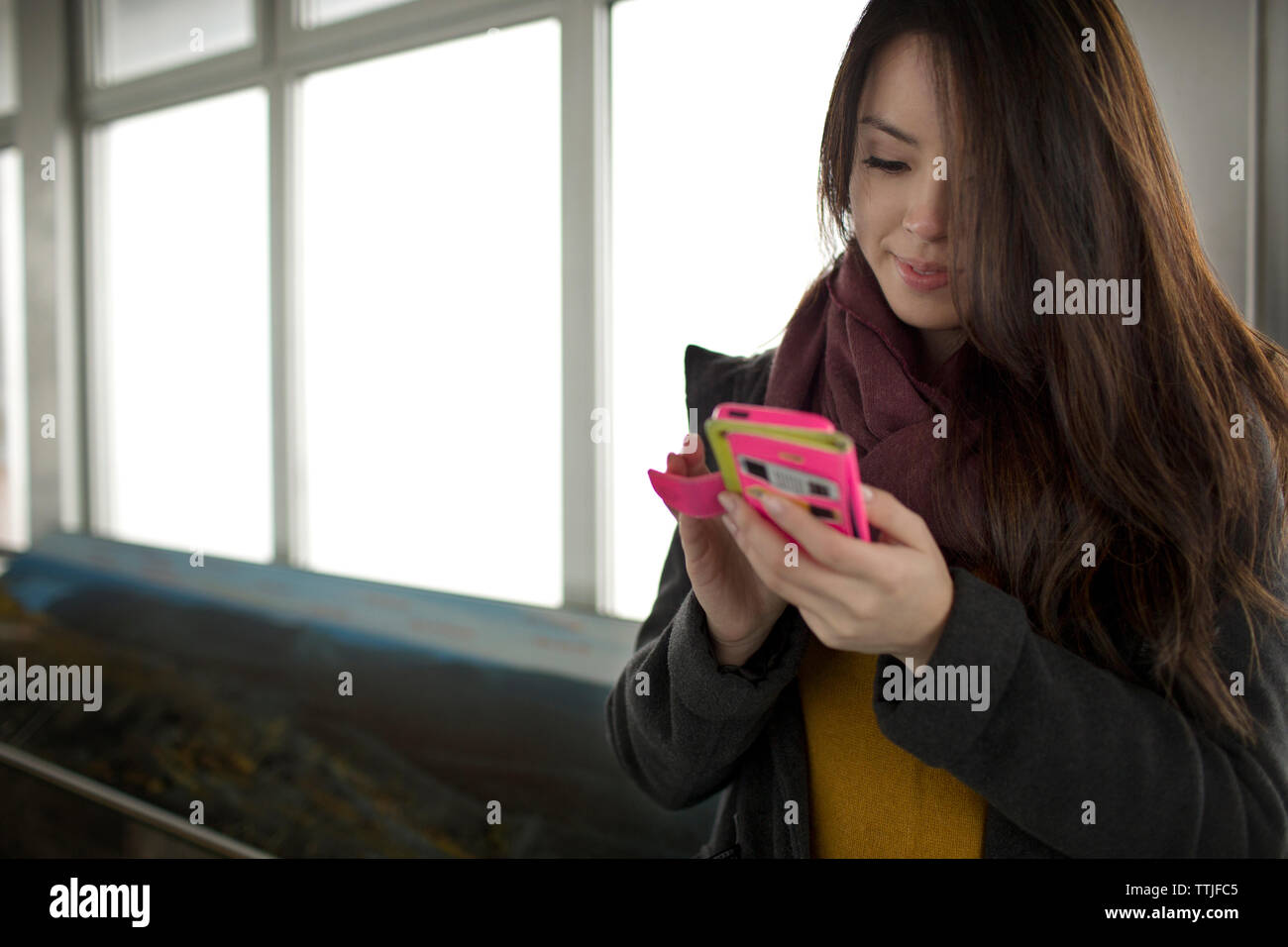 Donna che utilizza smart phone permanente, mentre dalla finestra Foto Stock