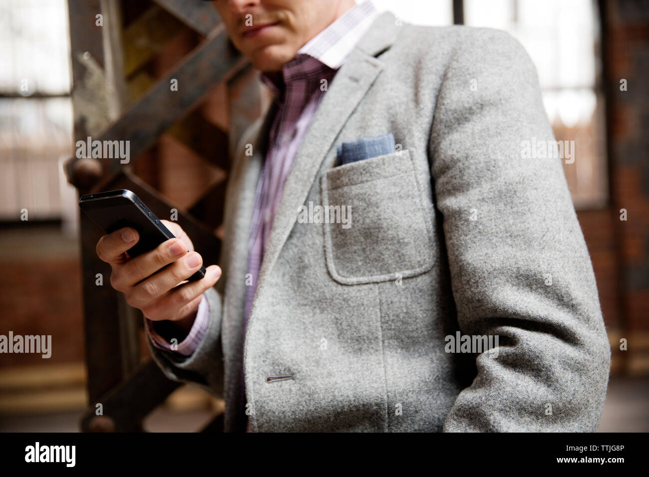 Sezione mediana di imprenditore utilizzando smart phone mentre in piedi in magazzino vuoto Foto Stock
