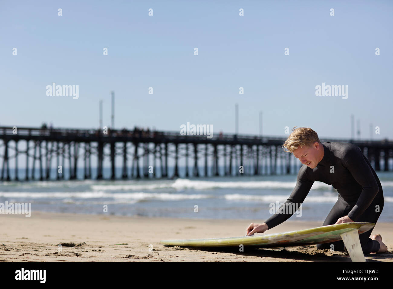 L'uomo la preparazione per il surf mentre inginocchiato alla spiaggia Foto Stock