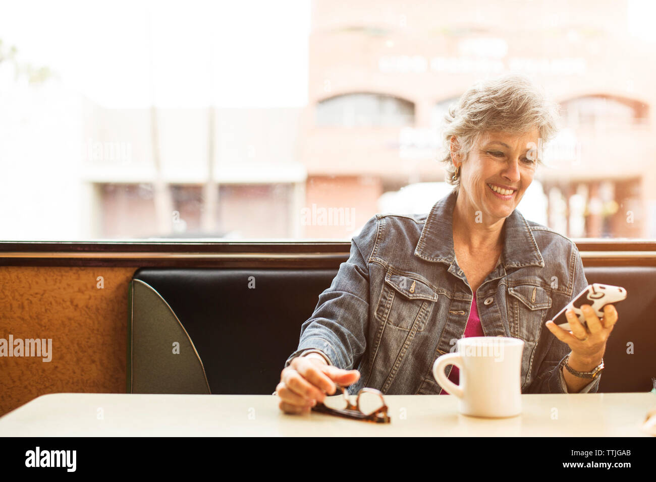 Donna che utilizza il telefono cellulare mentre è seduto presso il cafe Foto Stock